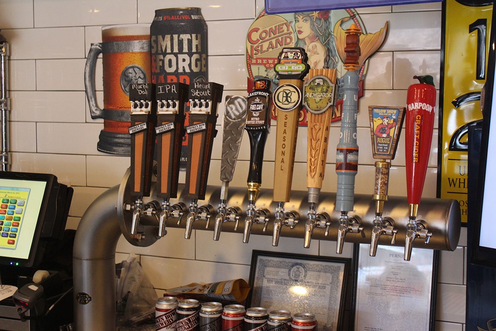 multiple beer taps behind a bar, A bar with numerous beer taps and a computer for ordering drinks.